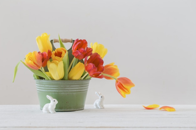 Red and yellow tulips in bucket and ceramic rabbit on white background