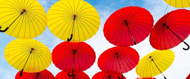 Красные и желтые зонтики висят на фоне неба снизу вверх