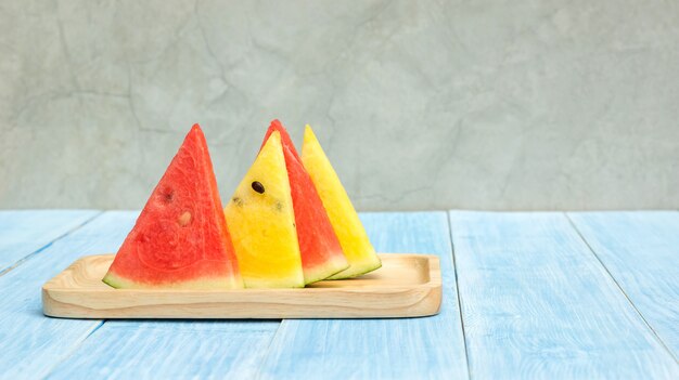 Photo red and yellow watermelon on a plate and blue wooden table.