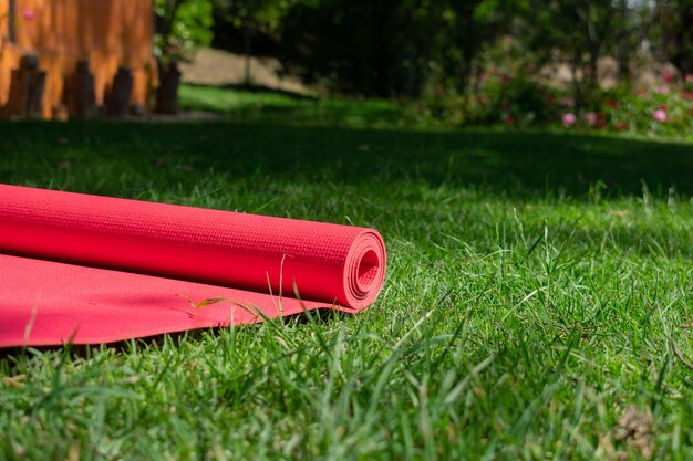 Foto mat da yoga rosso arrotolato sull'erba verde nel giardino da vicino concetto di fitness e benessere