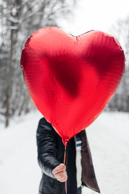 Красный шар в форме сердца в мужской руке в зимнем лесу