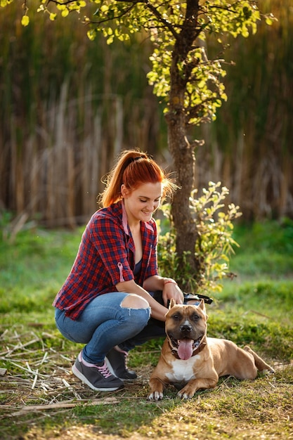 Redhair jouful giovane donna che accarezza il loro cane indossando abbigliamento sportivo godendo il loro tempo e le vacanze nel soleggiato parco