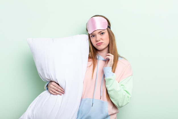 Рыжеволосая женщина чувствует стресс, тревогу, усталость и разочарование в пижаме и концепции подушки