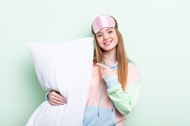 Redhair woman looking excited and surprised pointing to the side. pajamas and pillow concept