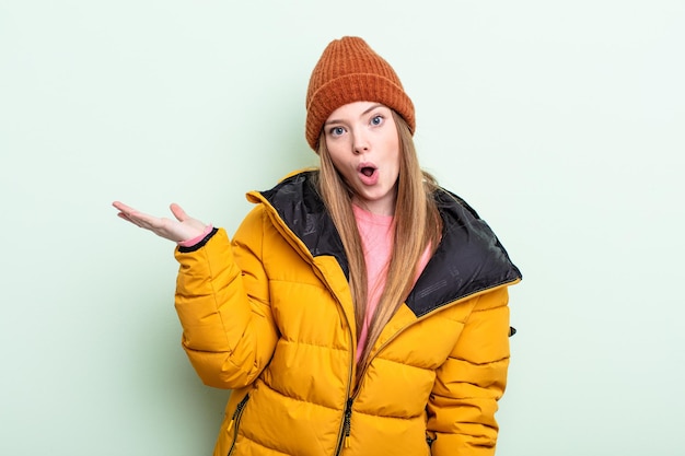 Redhair woman looking surprised and shocked, with jaw dropped holding an object. winter concept