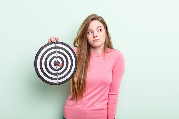 Foto donna dai capelli rossi che scrolla le spalle, sentendosi confusa e incerta. concetto di dardo diana