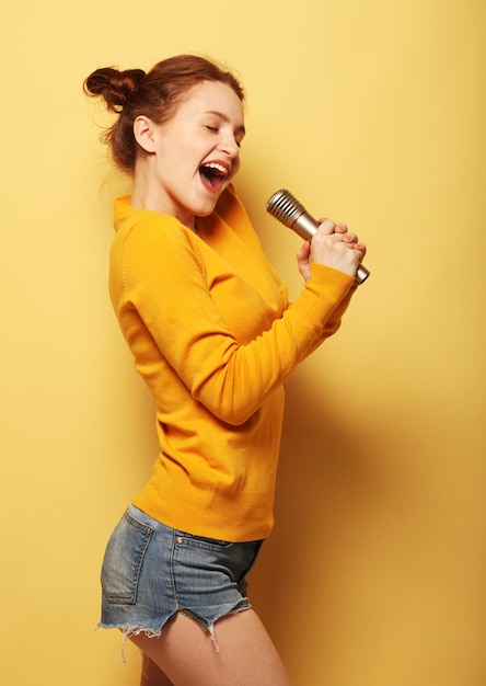 Foto redhair donna che canta karaoke isolato su sfondo giallo