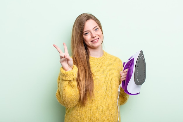 Redhair woman smiling and looking friendly, showing number two. iron clothes concept