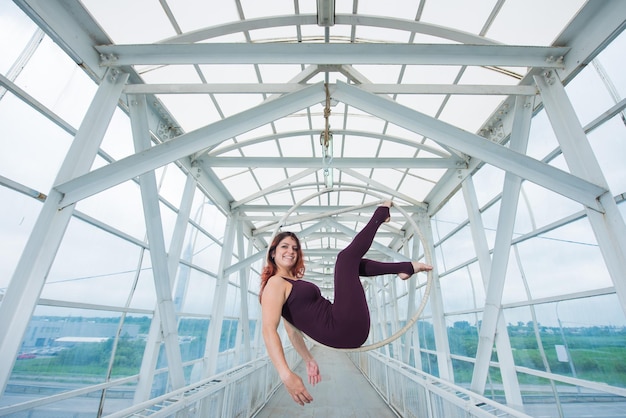 the redhaired aerial gymnast in a sports combo performs at the air hoop in a pedestrian crossing air acrobat hangs on an air ring suspended on a metal truss