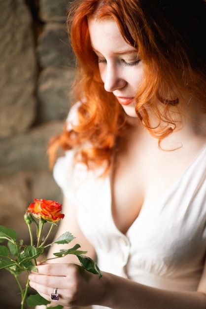 Redhaired beautiful girl near the old window in a white night dress in a French traditional house the theme of romance