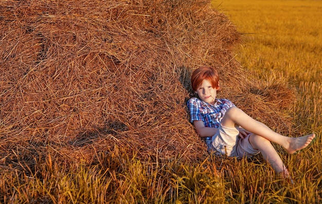 A redhaired boy leaning against a haystack on a lazy summer evening at sunset