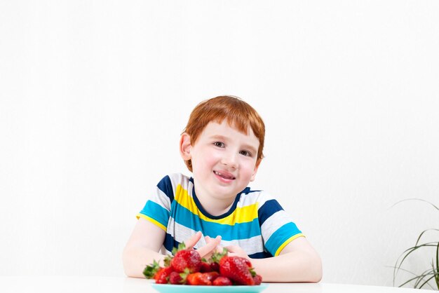 Redhaired boy with ripe red strawberries closeup portrait of a child during dessert