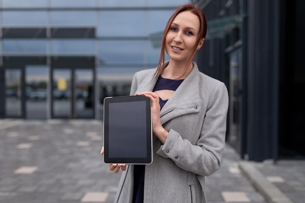 Redhaired business woman demonstrates the screen of the tablet on the background of the office