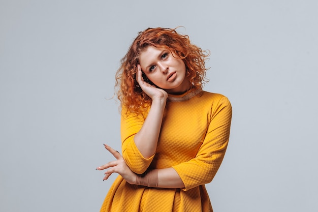 Redhaired curly girl Thinks on a light gray background