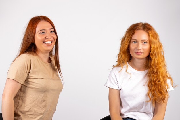 Redhaired cute womanfriends on a white wall smiling and posing