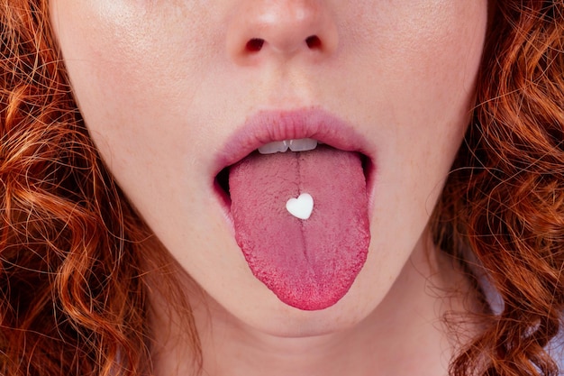 Photo redhaired ginger afro curly perfect skin woman taking happy love pills in studio yellow background .heart shape pill on females tongue.