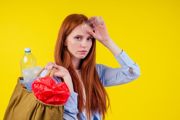 Redhaired ginger european woman with cotton eco bag full of
plastic trash in yellow studio backgroundrecycling ecology solution
concept