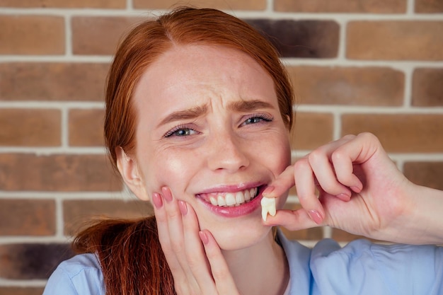 Redhaired ginger female with pain grimace holding white wisdom tooth after surgery removal extracted of a tooth