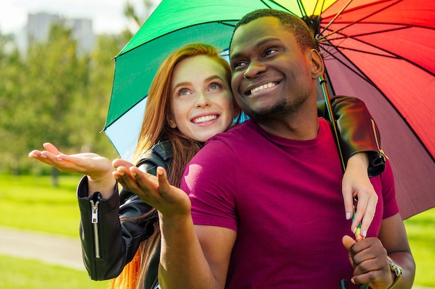 Redhaired ginger woman and african american man standing close to each other under umbrella in summer park