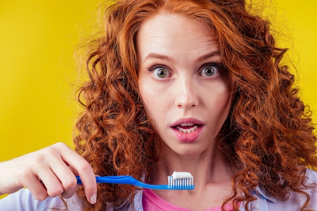 Redhaired ginger woman brushing teeth with toothpaste eco paste on yellow studio background.