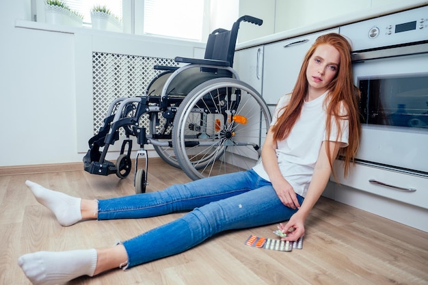 Redhaired ginger woman falling down and crawling for help in\
kitchen room ,holding pills in hands.