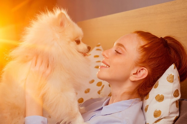 Redhaired ginger woman having fun with her fluffy spitz at room sunset light background.