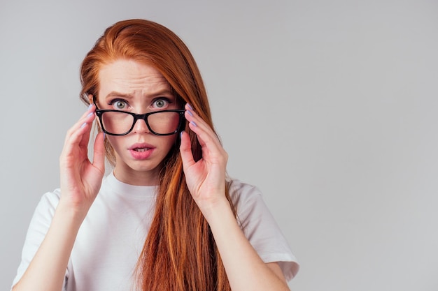 Redhaired ginger woman wearing glasses and white cotton eco t-shirt in gray studio background.