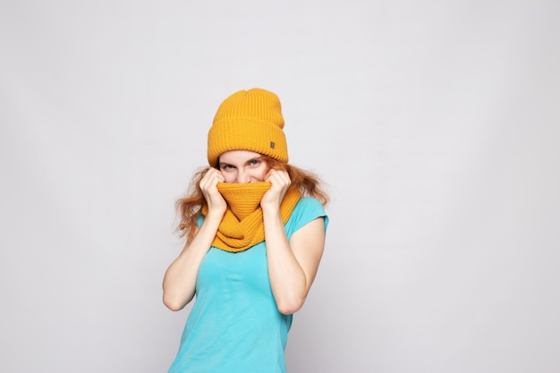 Redhaired girl in a warm hat on a light background