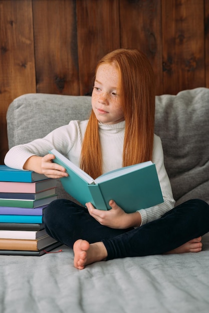 A redhaired girl with a book in her hands sits in the lotus position and reads