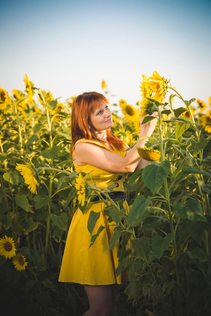 A redhaired girl in a yellow dress in sunflowers