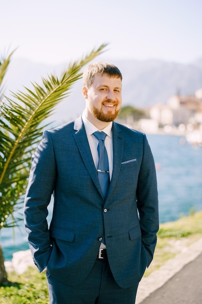 Redhaired man in a blue suit stands near a palm tree portrait