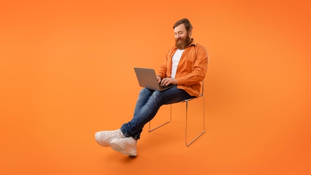 Redhaired programmer guy sits typing on his laptop orange background