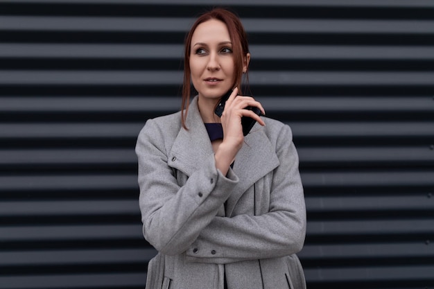 Redhaired seriously businessman with a mobile phone in a coat against the background of a relief