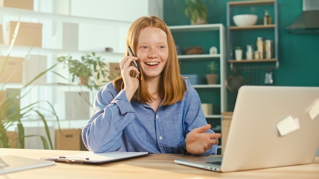 Redhaired teenage girl studying at home online talking on the phone