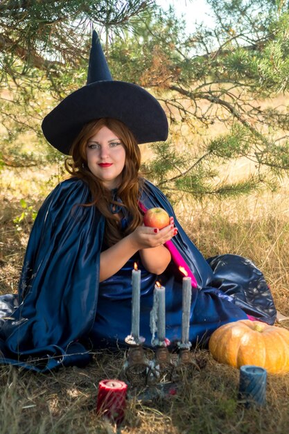 A redhaired witch in a pointed hat and cloak in the forest is telling fortunes over candles