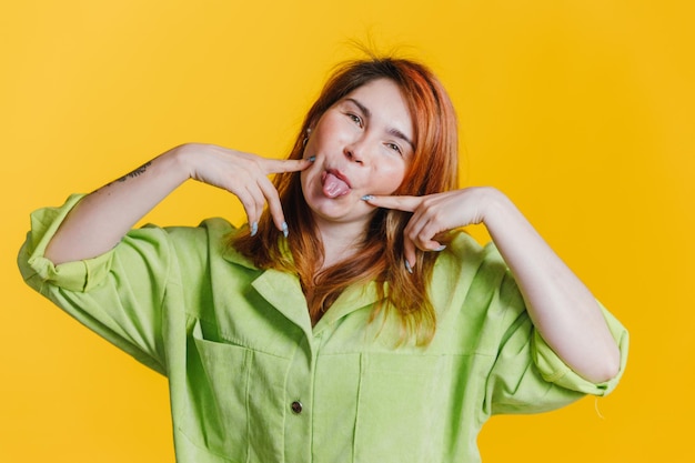 노란색 배경에 녹색 짧은 서 있는 redhaired 여자 웃 고 그녀의 혀를 보여주는