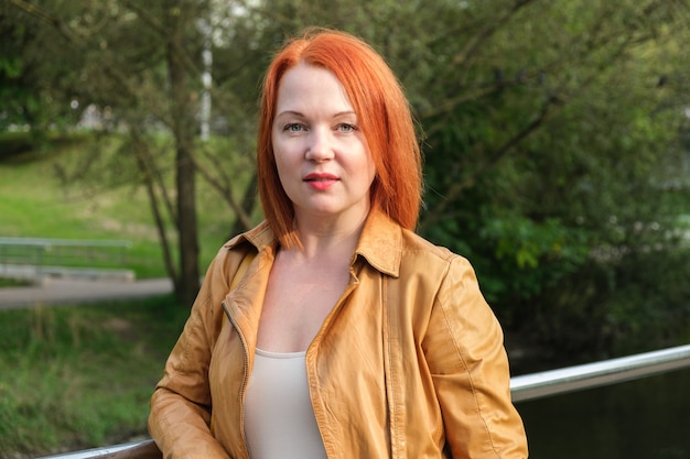 Redhaired woman in a leather jacket stands in a city park