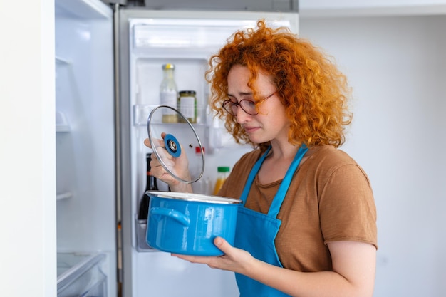 Photo redhaired woman meticulously inspects the fridge for spoiled food her discerning eyes and cautious demeanor ensure freshness capturing the essence of responsible and mindful food management