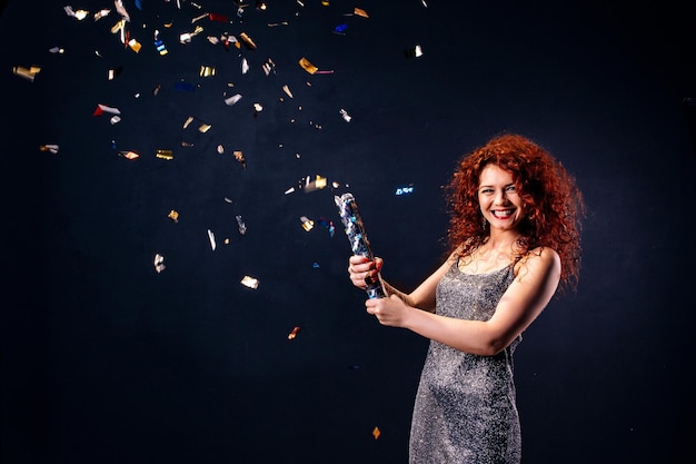 Foto donna dai capelli rossi in festa che ride mentre fa saltare in aria la parete popper della festa della festa del compleanno di capodanno