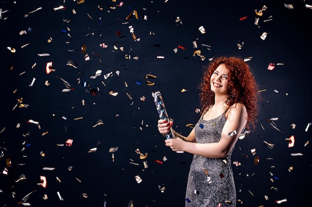 Foto donna dai capelli rossi in festa che ride mentre fa saltare in aria la parete popper della festa della festa del compleanno di capodanno