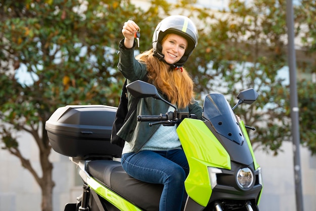 Donna dai capelli rossi in sella a una moto su una strada cittadina che mostra le chiavi