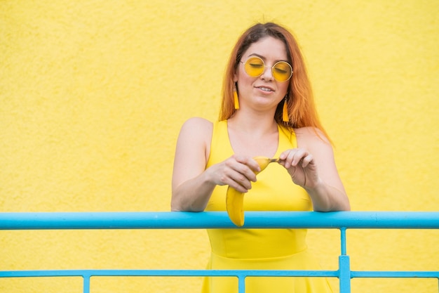 Redhaired woman in sunglasses holds a banana on a yellow background