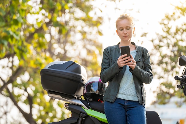 駐車中のオートバイの横でスマートフォンを使用している赤毛の女性