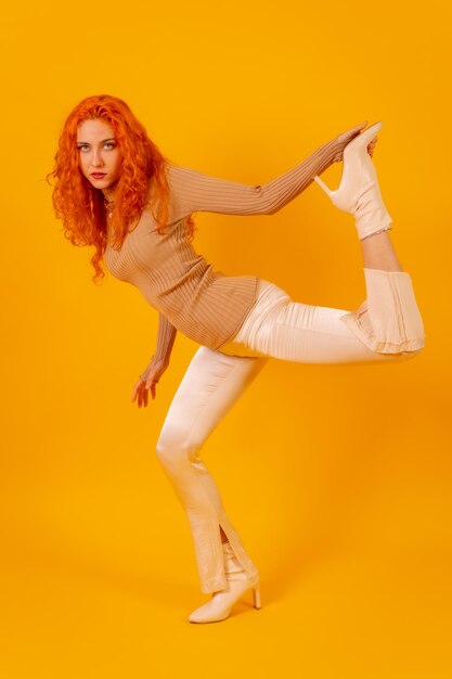 Redhaired woman on a yellow background studio shot fashion posed full body in white boots