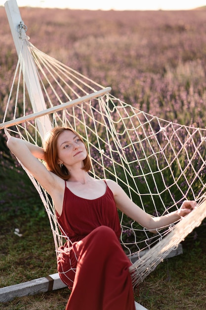 A redhaired young girl without makeup is resting on a hammock in a lavender field Summer vacation and travel time