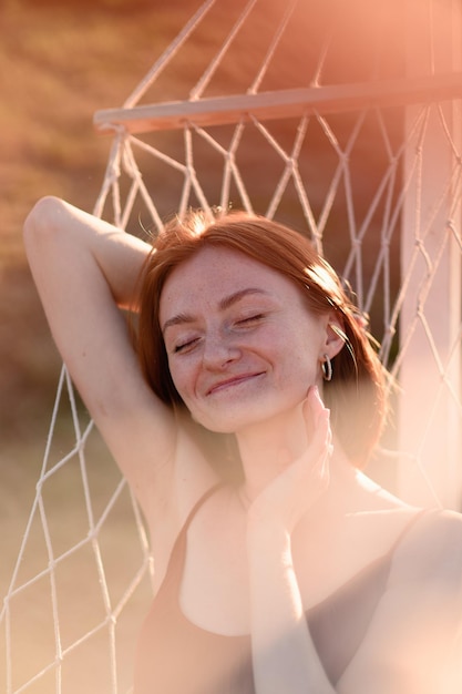 ラベンダー畑のハンモックで休んでいる化粧をしていない赤毛の若い女の子 夏休みと旅行の時間