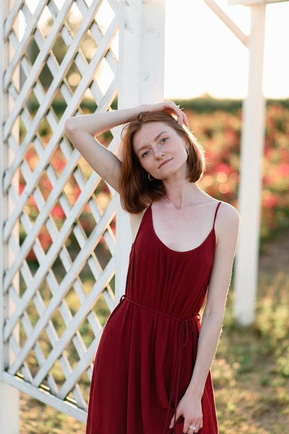 A redhaired young girl without makeup is resting near the gazebo in a flower field Summer vacation and travel time