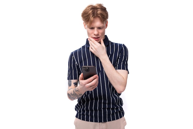 Redhaired young man in a blue tshirt on a white background with a mobile phone in his hands