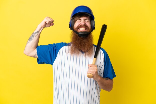Redhead baseball player man with helmet and bat isolated on yellow background doing strong gesture