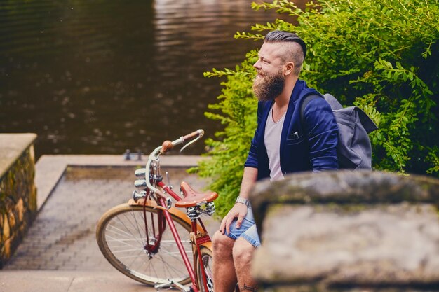 Maschio hipster barbuto rosso su una bicicletta retrò in un parco estivo.